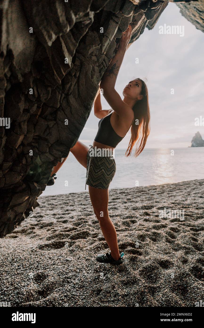 Sport Donna arrampicata sulla roccia. Giovane donna con corpo slim-fit arrampicata in grotta vulcanica basalto con bella vista mare. La ragazza atleta si allena Foto Stock