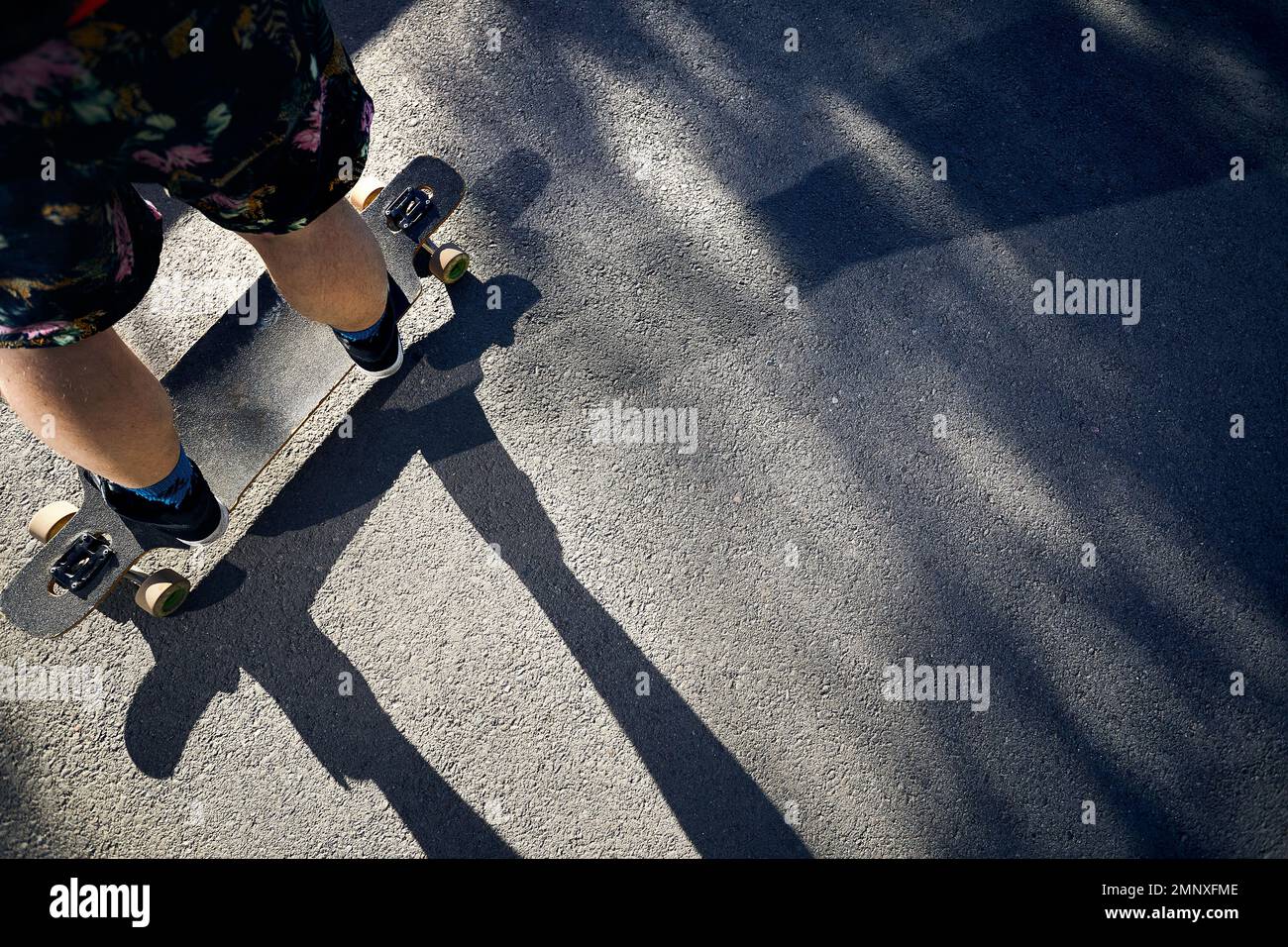 Uomo Skater al suo longboard sulla strada di montagna primo piano girato al mattino luce del sole e ombra dura Foto Stock