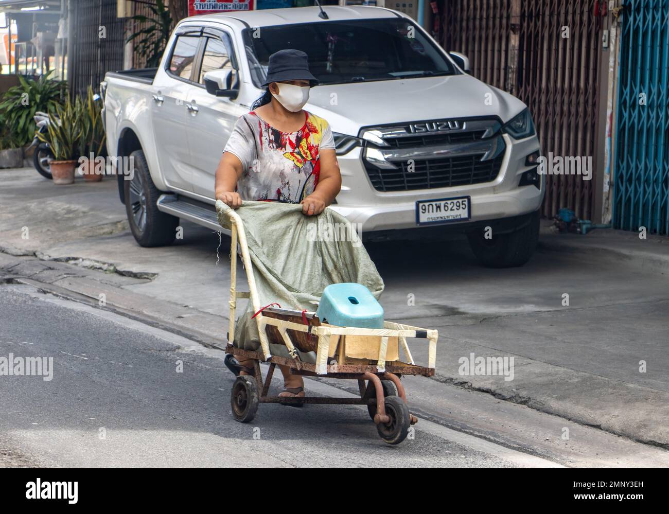 BANGKOK, THAILANDIA, DEC 06 2022, Una donna con una maschera spinge un carrello a tre ruote con carico sulla strada Foto Stock