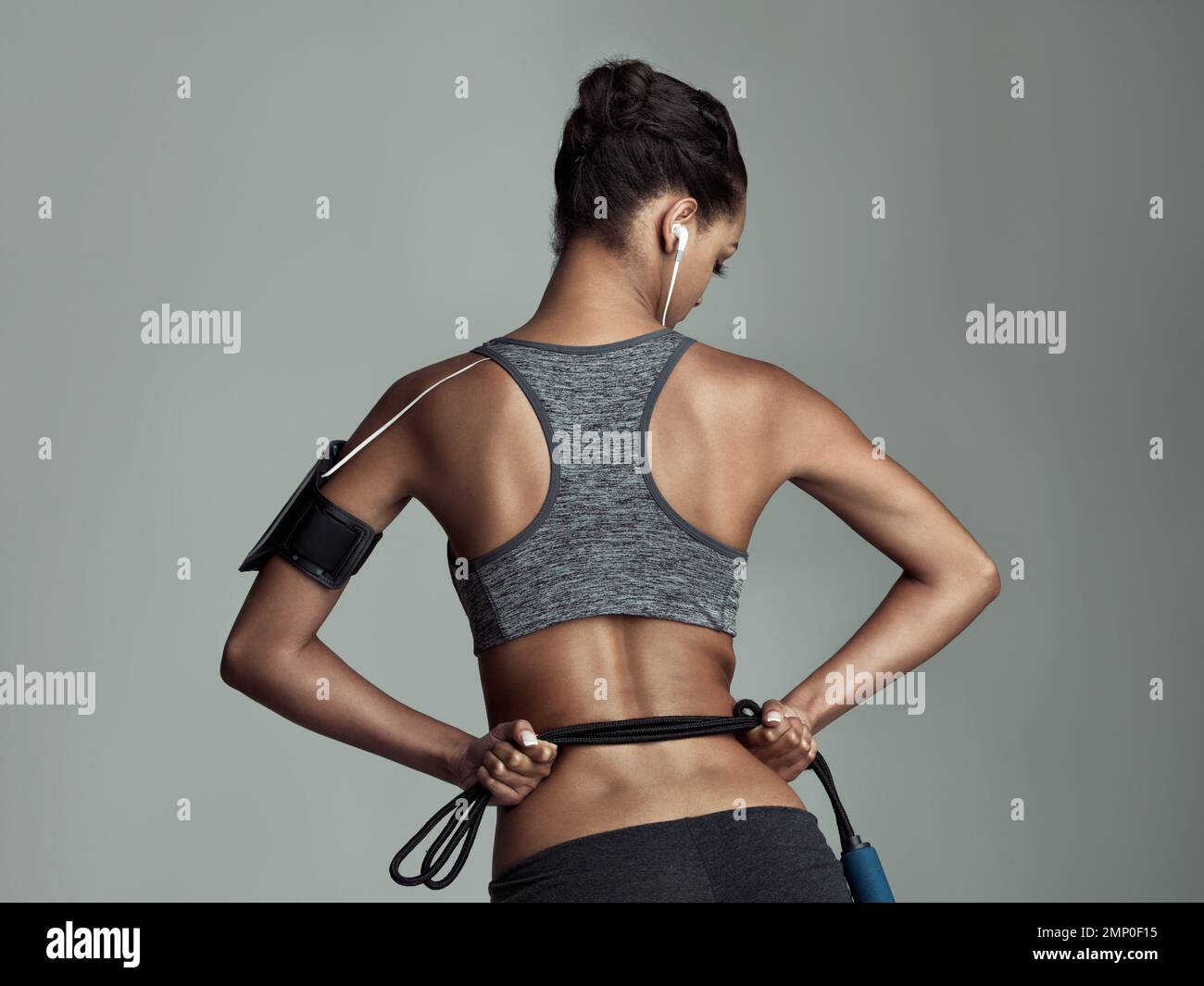 Tutto ciò di cui ha bisogno per un ottimo allenamento. Ripresa da studio con vista posteriore di una giovane donna che tiene una corda su uno sfondo grigio. Foto Stock