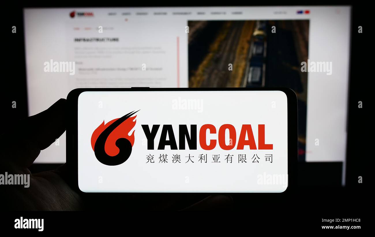 Persona in possesso di smartphone con il logo della società mineraria Yancoal Australia Limited sullo schermo di fronte al sito Web. Messa a fuoco sul display del telefono. Foto Stock