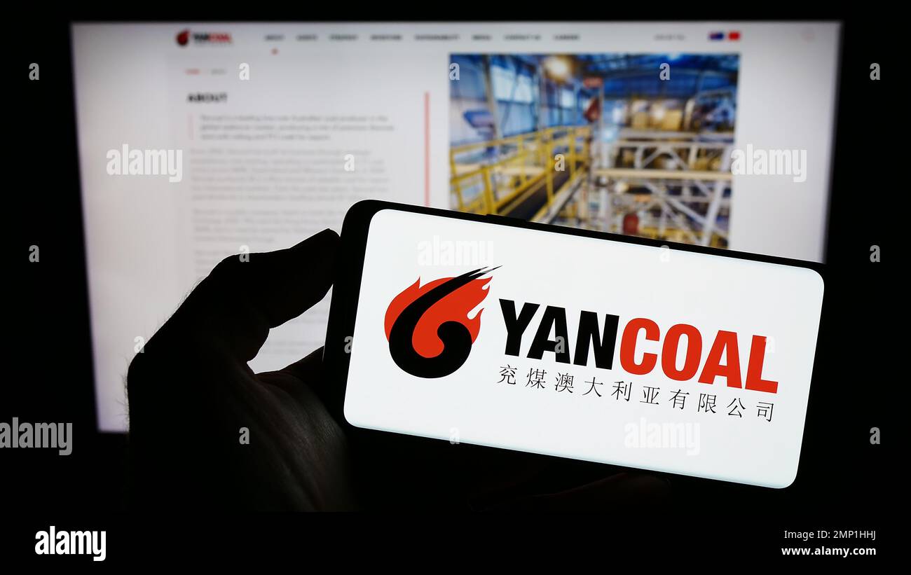Persona che tiene il telefono cellulare con il logo della società mineraria di carbone Yancoal Australia Limited sullo schermo di fronte alla pagina web. Messa a fuoco sul display del telefono. Foto Stock