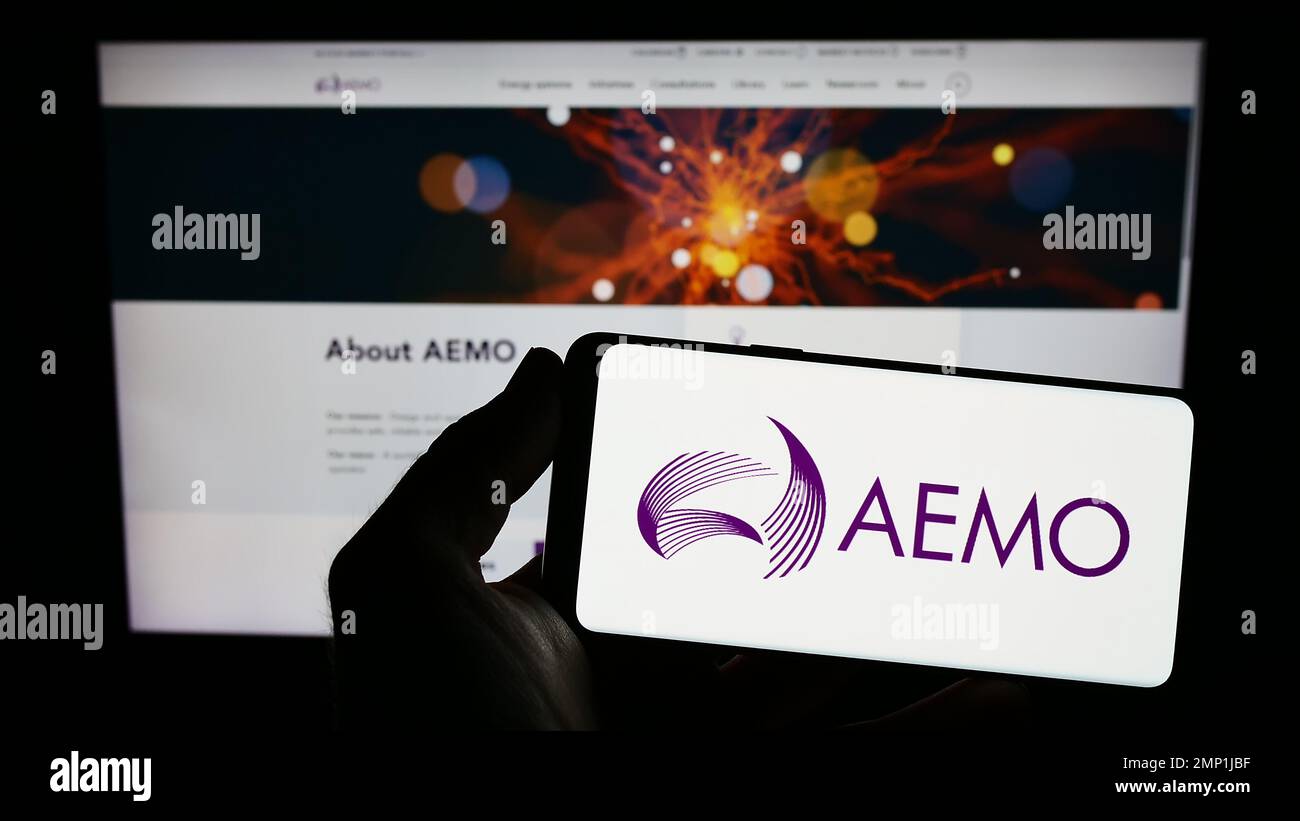 Persona che tiene in mano uno smartphone con il logo dell'operatore australiano del mercato dell'energia (AEMO) sullo schermo di fronte al sito Web. Messa a fuoco sul display del telefono. Foto Stock