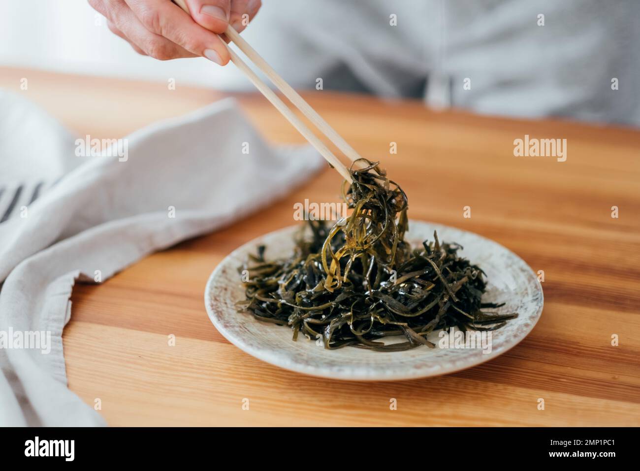 Insalata di alghe sul tavolo l'uomo mangia con bacchette insalata di laminaria preparata a casa Foto Stock