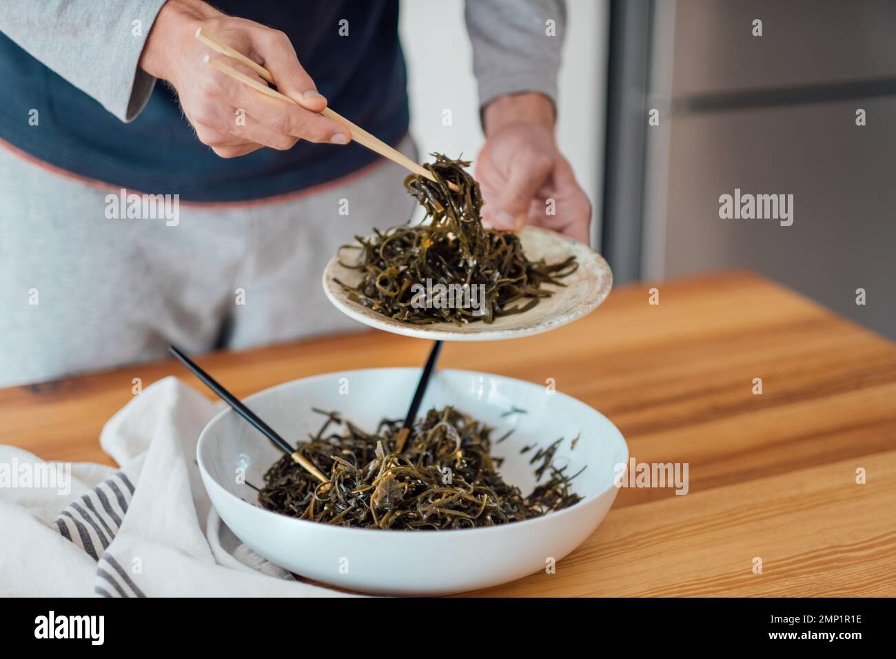 Insalata di alghe sul tavolo l'uomo mangia con bacchette insalata di laminaria preparata a casa Foto Stock
