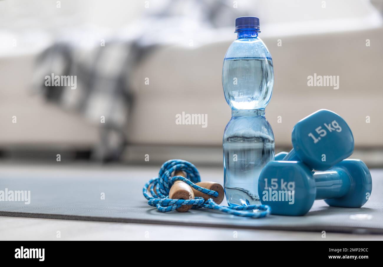 Una corda da salto, manubri e una bottiglia d'acqua su un tappetino a casa nel soggiorno. Concetto di stile di vita sano. Foto Stock
