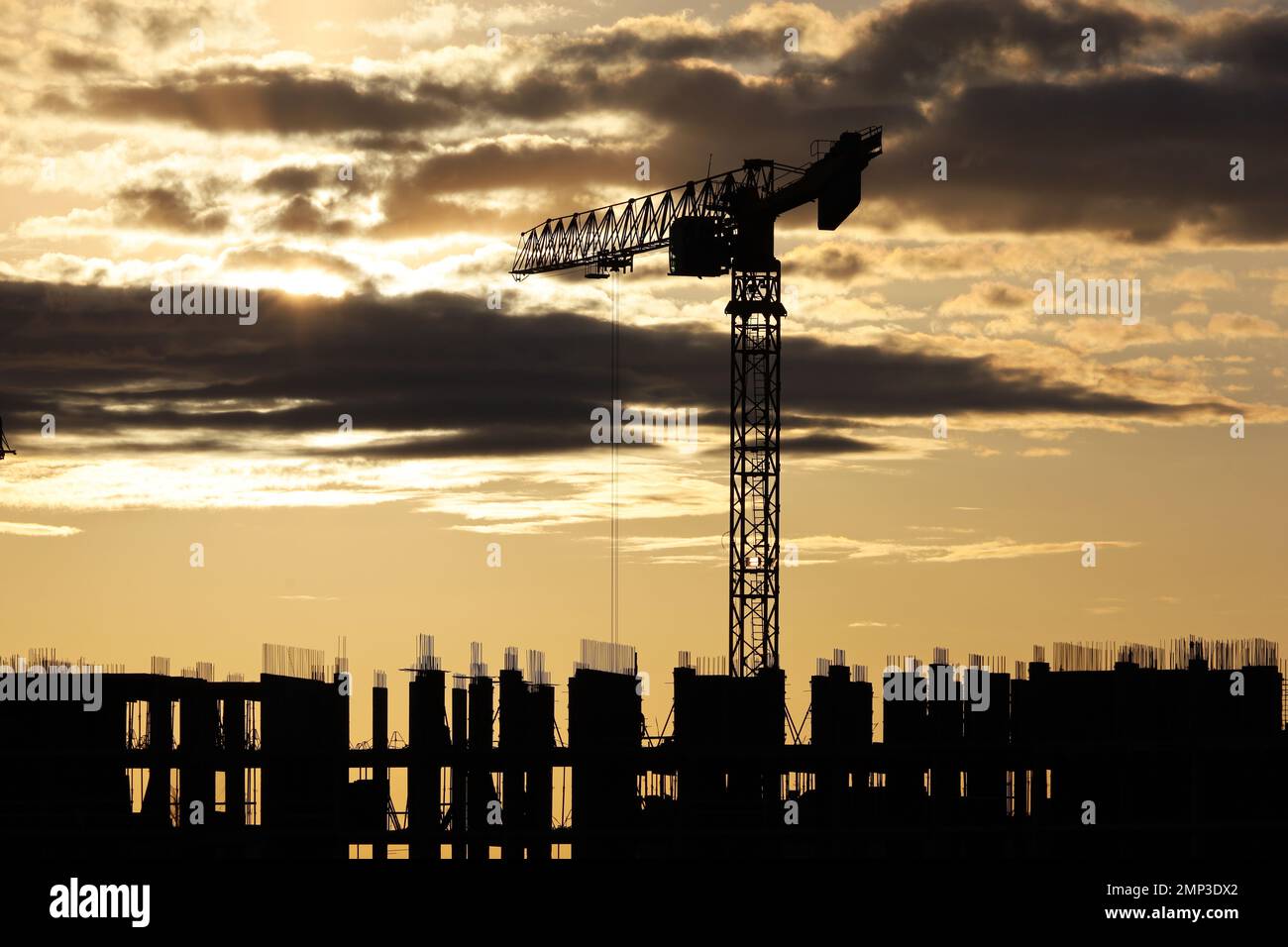 Silhouette di gru a torre e impalcatura di edifici infiniti all'alba. Edilizia abitativa, condominio in città Foto Stock