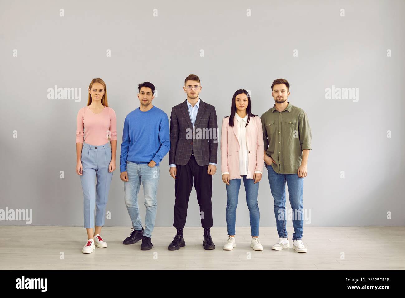 Ritratto di gruppo di cinque giovani seri in abiti casual eleganti in piedi in studio Foto Stock