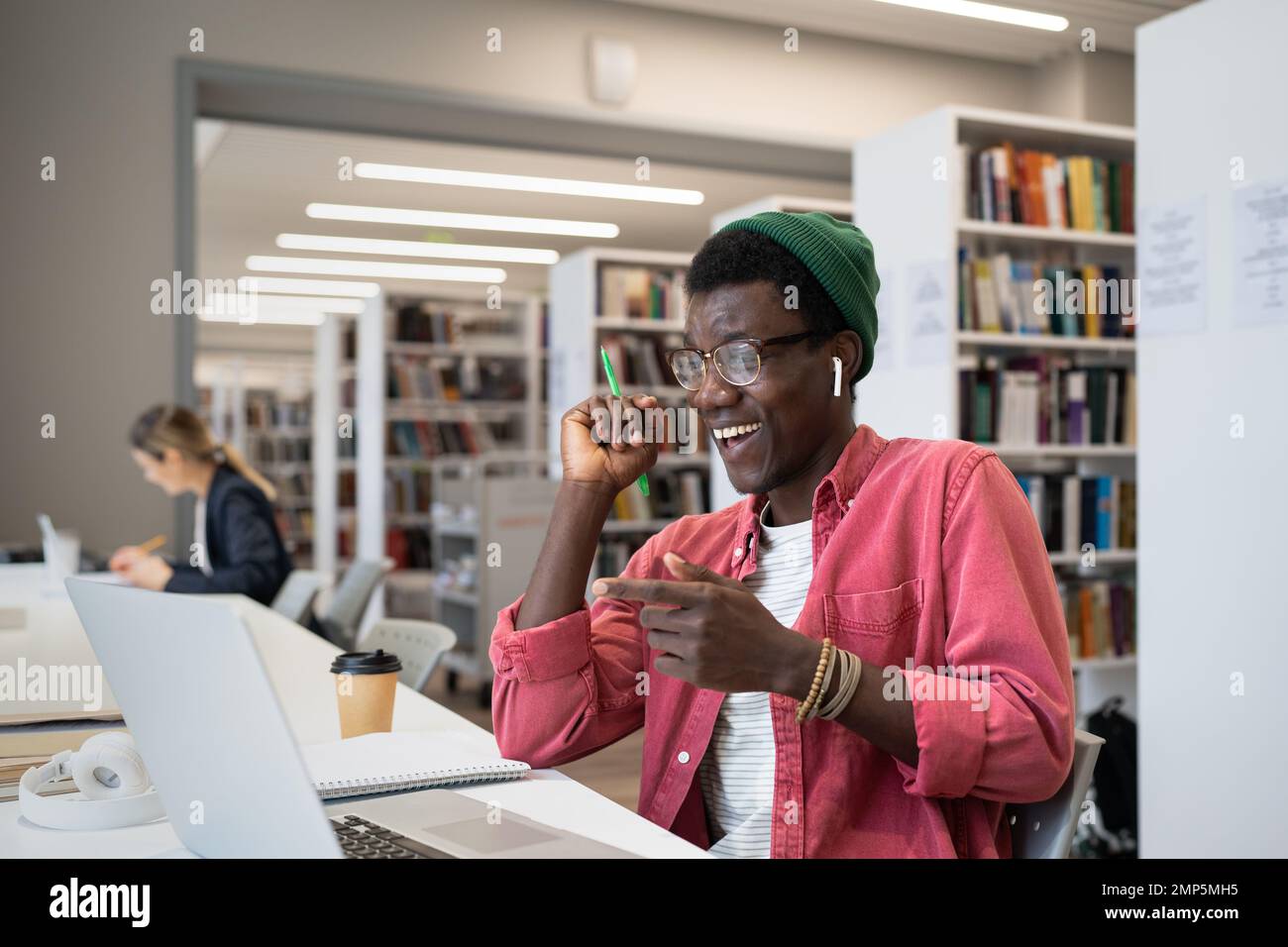 Un giovane tutor afro-americano che indossa auricolari che conducono una lezione online in biblioteca Foto Stock