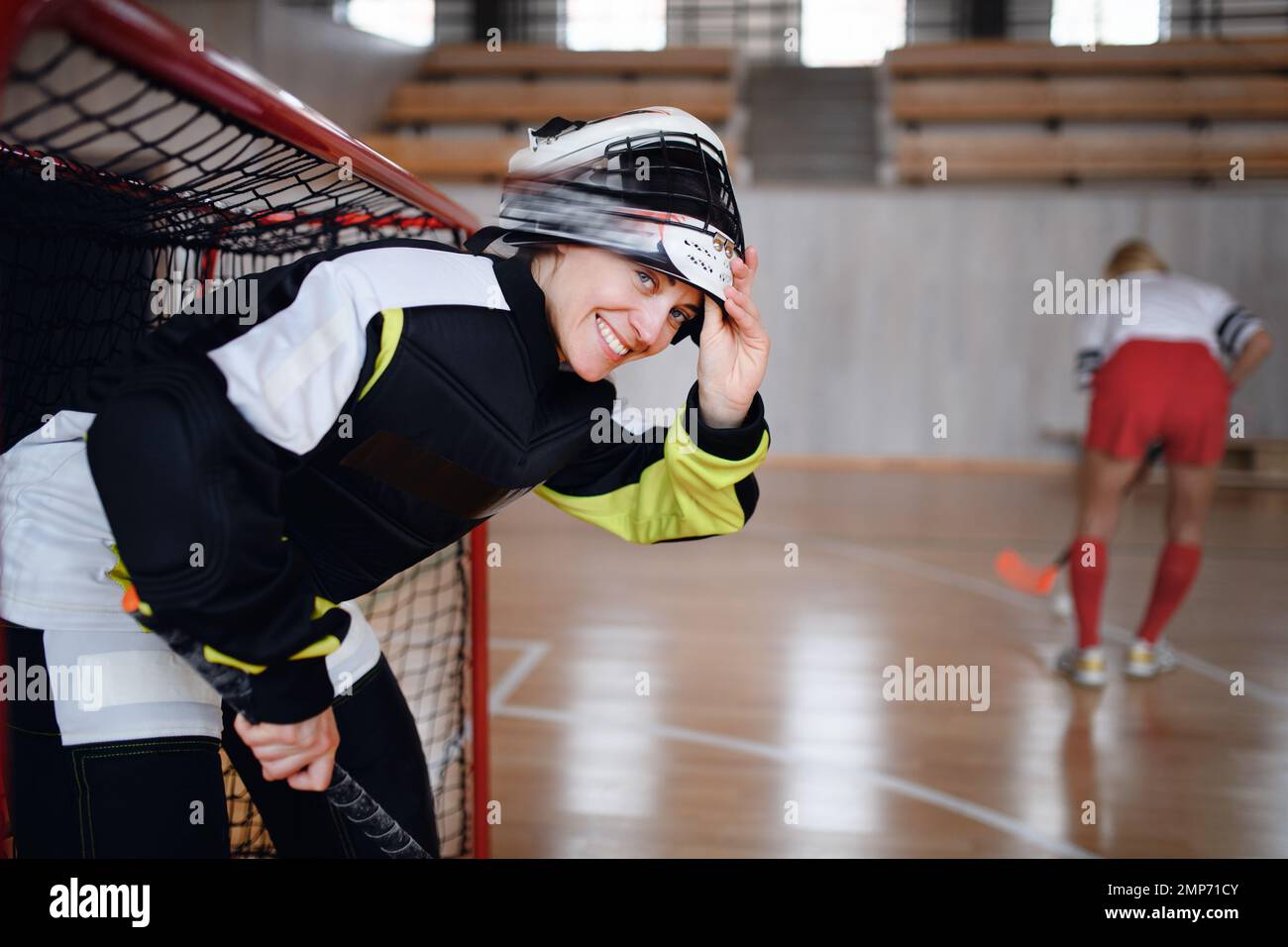 Primo piano di donna portiere di floorball in casco concettando su gioco in palestra. Foto Stock