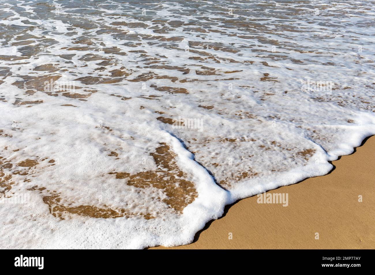 Onde schiumose che si infrangono dolcemente su una spiaggia di sabbia di primo piano. Bournemouth, Dorset, Inghilterra Foto Stock