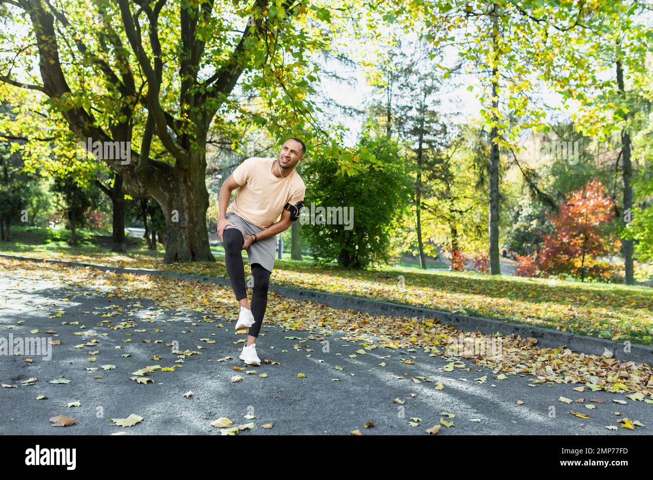 Giovane atleta afro-americano maschile che fa una corsa mattutina nel parco. Ferì il ginocchio, allungò i muscoli, si alza tenendo la gamba, sente dolore grave. Foto Stock