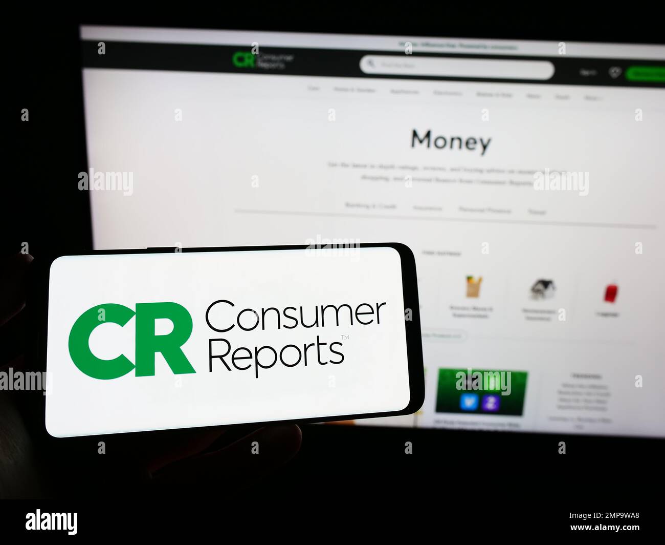 Persona che tiene in mano lo smartphone con il logo dell'organizzazione statunitense Consumer Reports (CR) sullo schermo davanti al sito Web. Messa a fuoco sul display del telefono. Foto Stock
