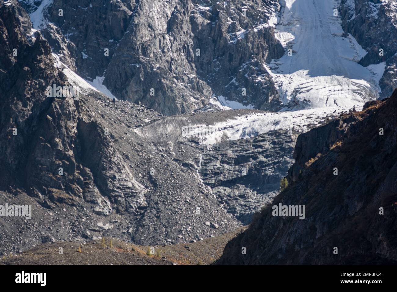 La lingua del ghiacciaio alpino Zelinsky con la neve scende da alte montagne rocciose in pietra tra le cime di Altai. Foto Stock