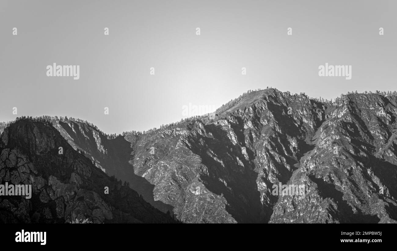 Foto in bianco e nero della cima delle scogliere di pietra con una foresta sullo sfondo del cielo ad Altai durante il giorno d'autunno. Foto Stock