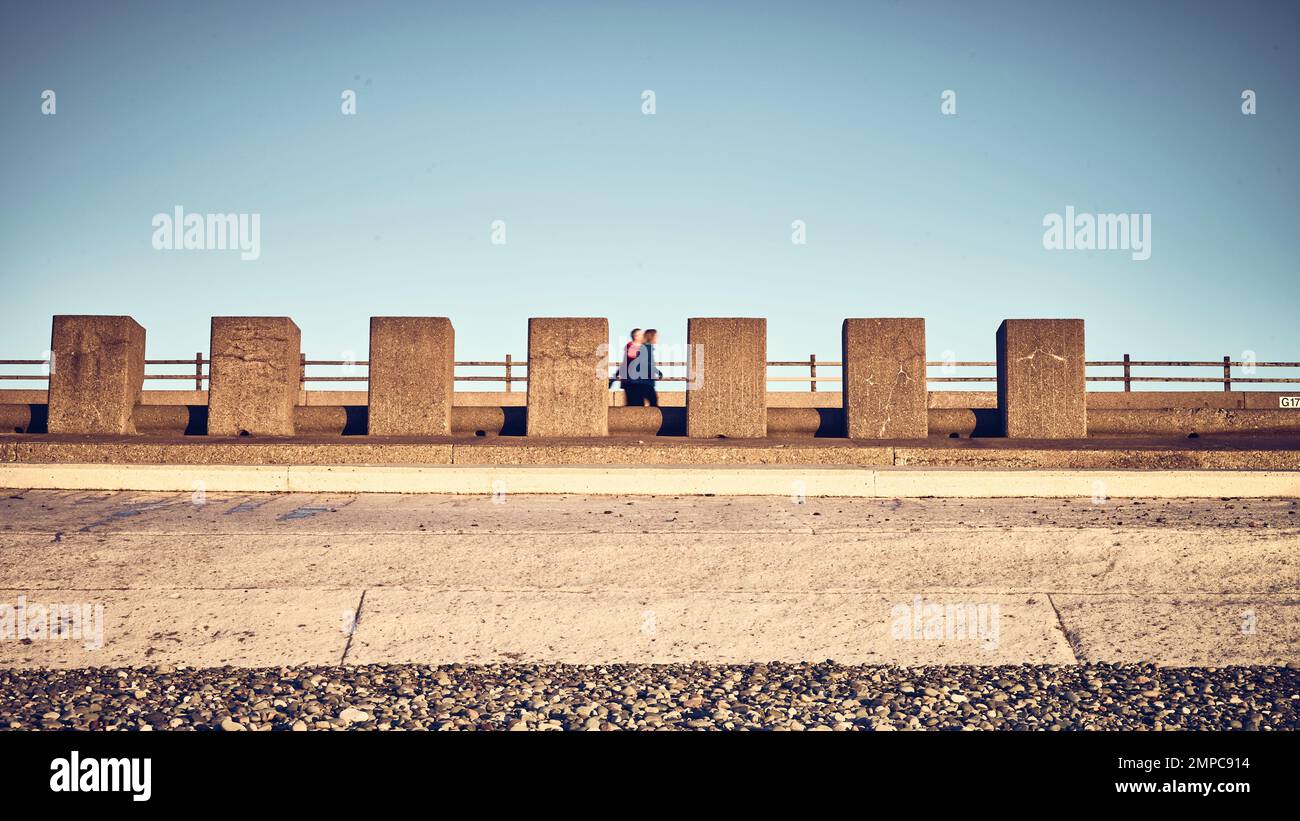 Persone che camminano accanto colonne di cemento sulla marina Rossall Foto Stock