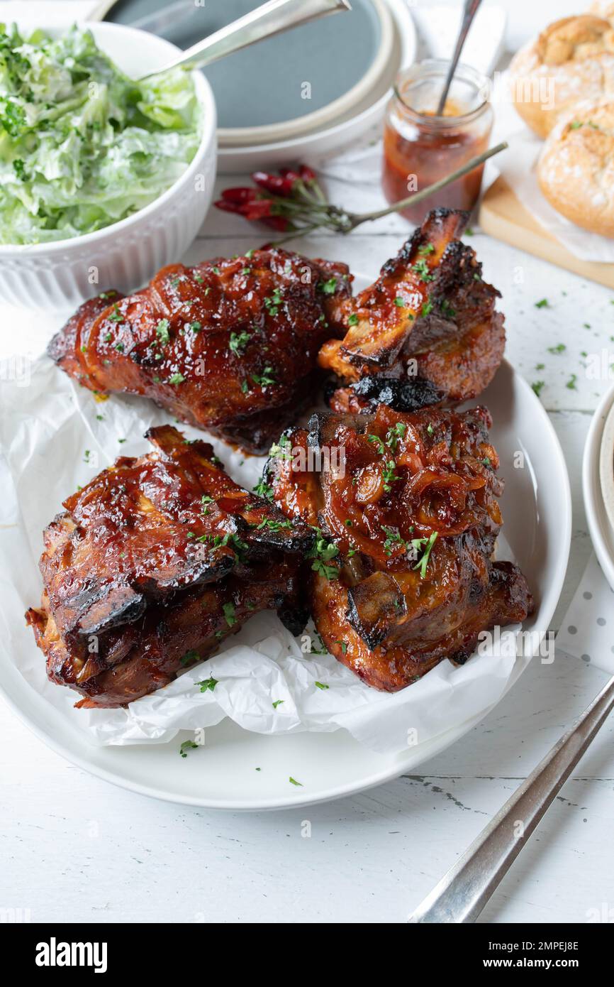Costolette di maiale alla griglia con salsa al barbecue e cipolle con insalata e pane sullo sfondo del tavolo da cucina Foto Stock
