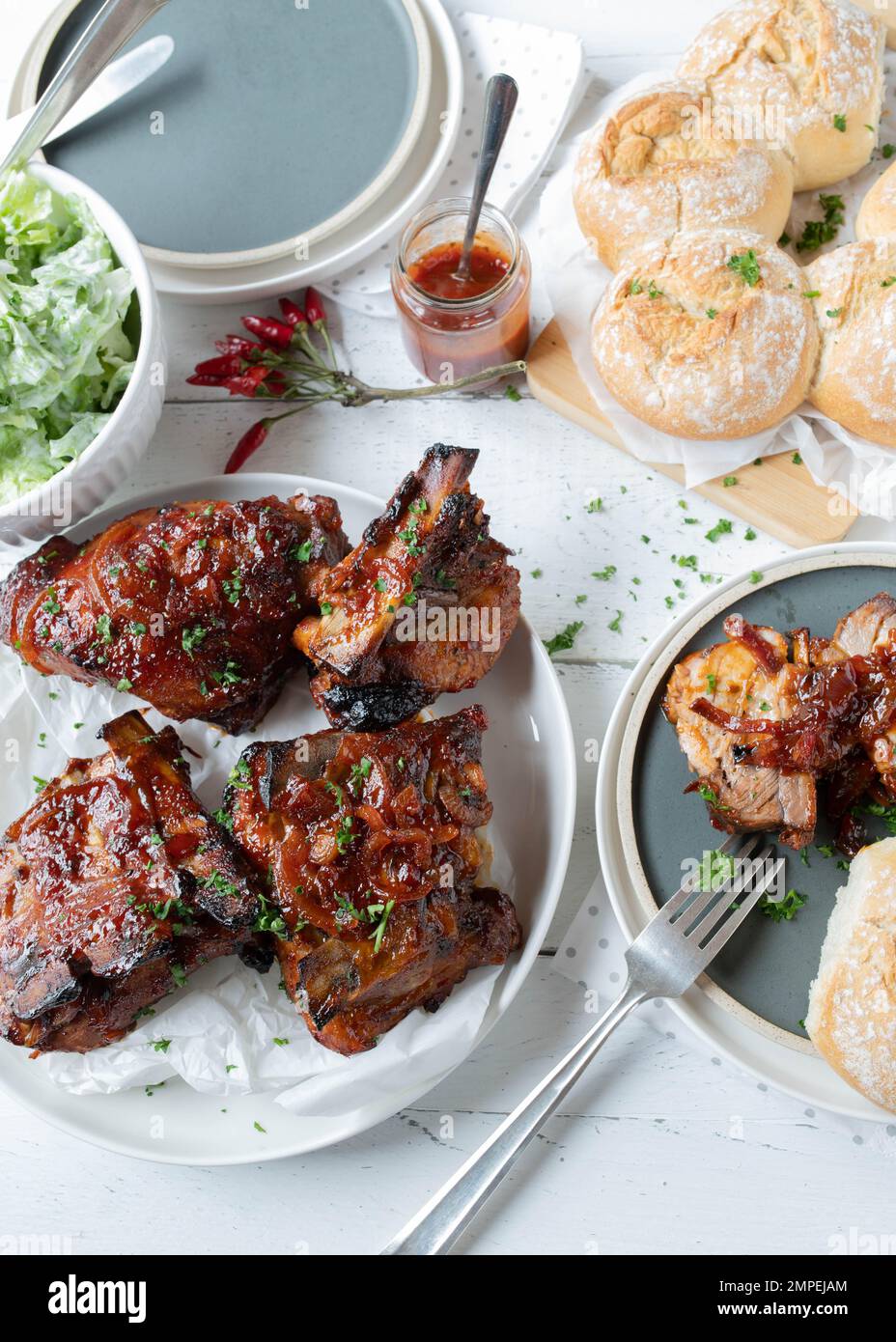 Costolette di maiale con salsa al barbecue e cipolle con insalata e pane sullo sfondo del tavolo da cucina Foto Stock