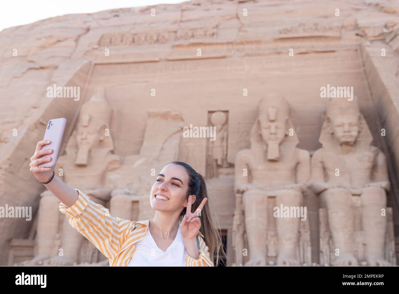 Felice giovane donna turista prendere un selfie con il famoso tempio di Abu Simbel sul retro Foto Stock