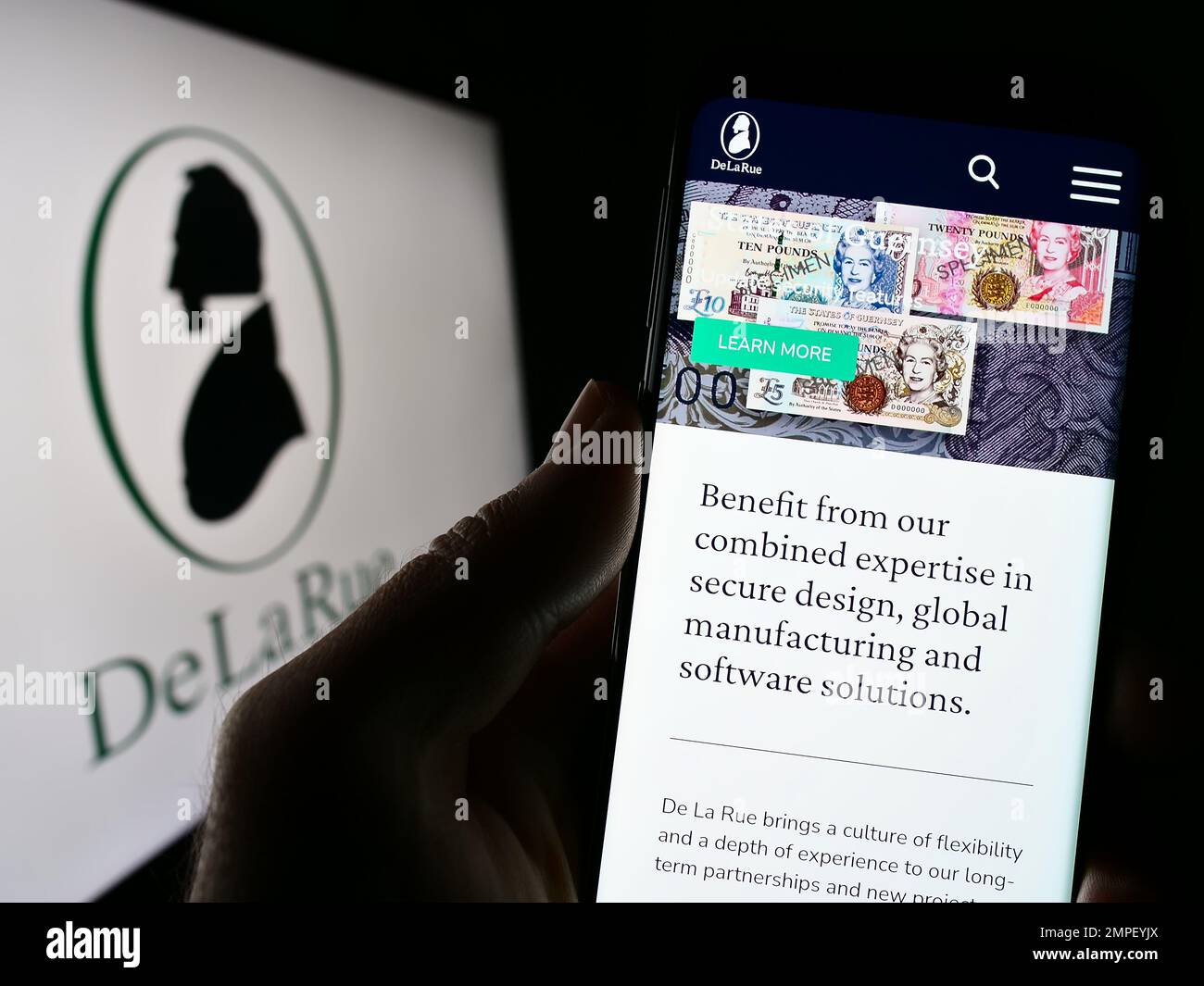 Persona che tiene uno smartphone con il sito web del produttore di banconote britanniche De la Rue plc sullo schermo di fronte al logo. Messa a fuoco al centro del display del telefono. Foto Stock