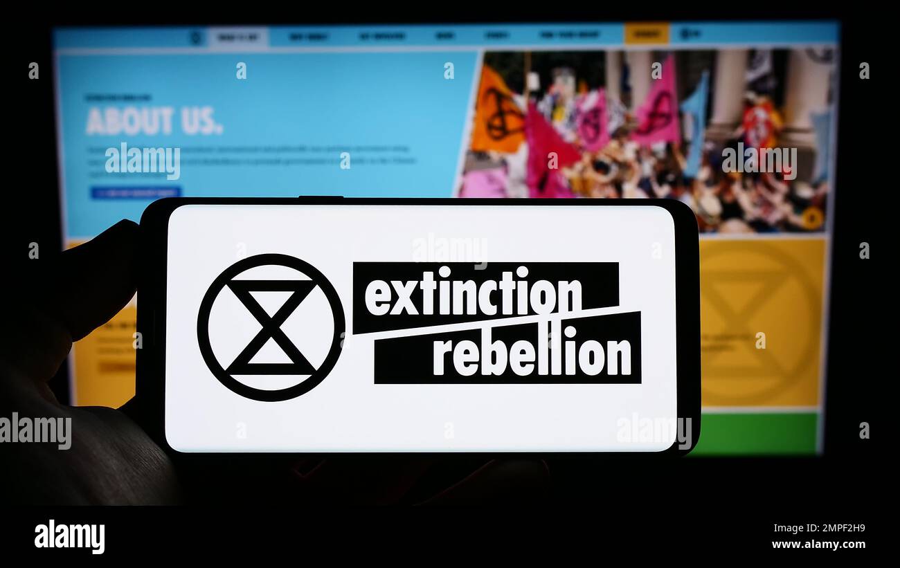 Persona che tiene uno smartphone con il logo dell'organizzazione Extinction Rebellion (XR) sullo schermo di fronte al sito Web. Messa a fuoco sul display del telefono. Foto Stock