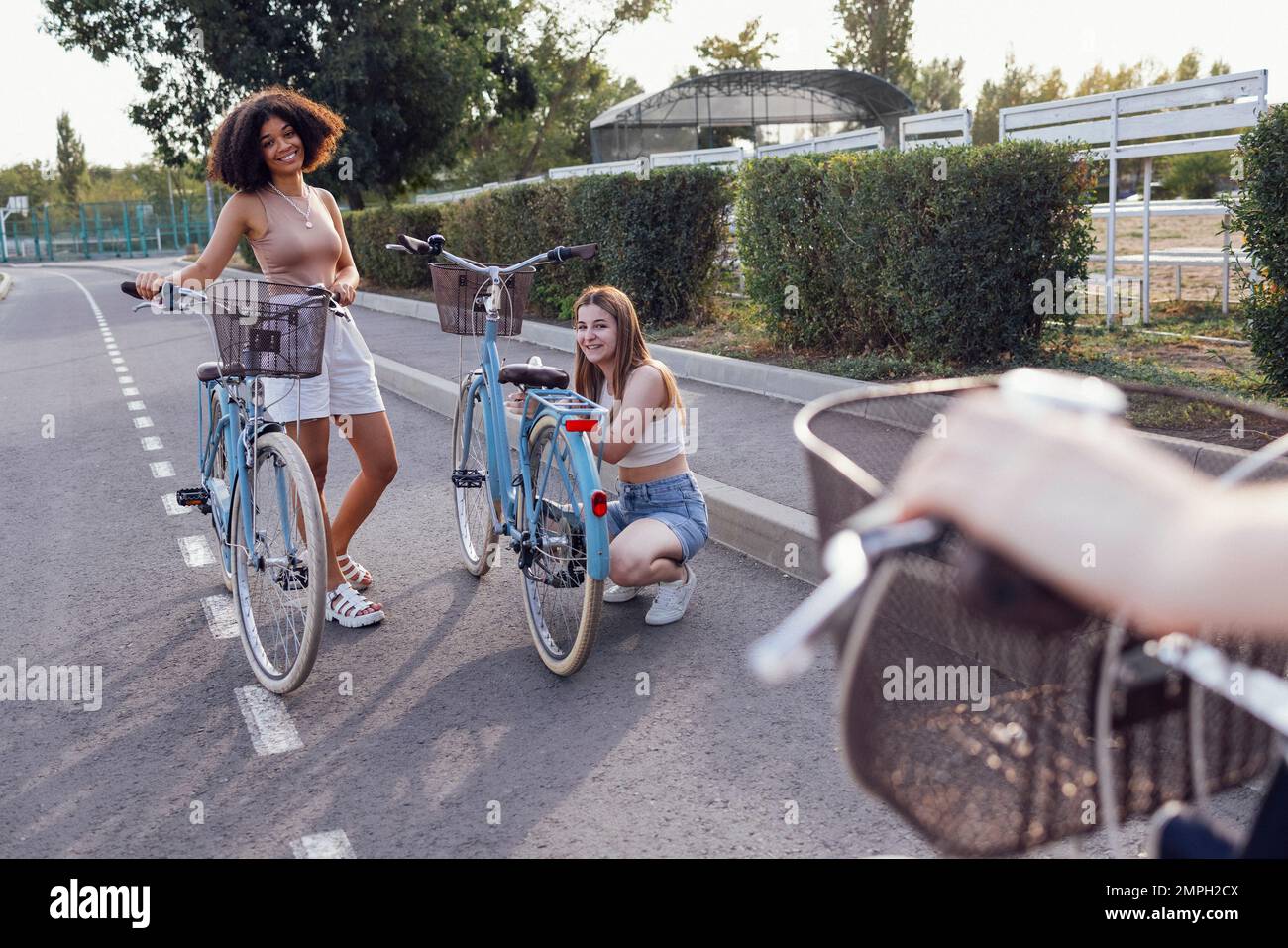 Adolescenti di diverse nazionalità e aspetto in bicicletta percorrono una strada cittadina. Le ragazze giovani e positive sorridono insieme. Stile di vita sano A. Foto Stock