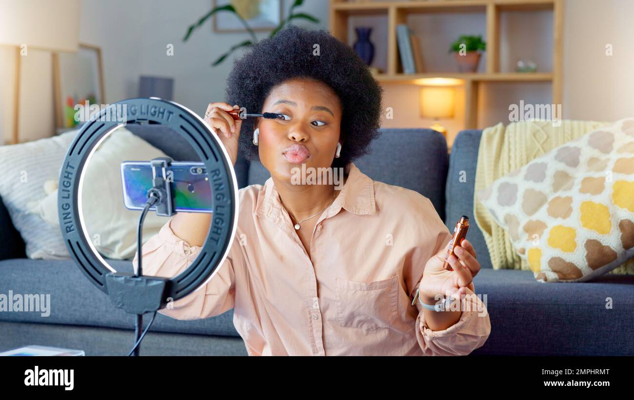 Afro Beauty Influencer, vlogger o podcast host parlare, utilizzando il telefono per filmare live streaming trucco tutorial con il nuovo makeup mascara. Donna eccitata usando Foto Stock