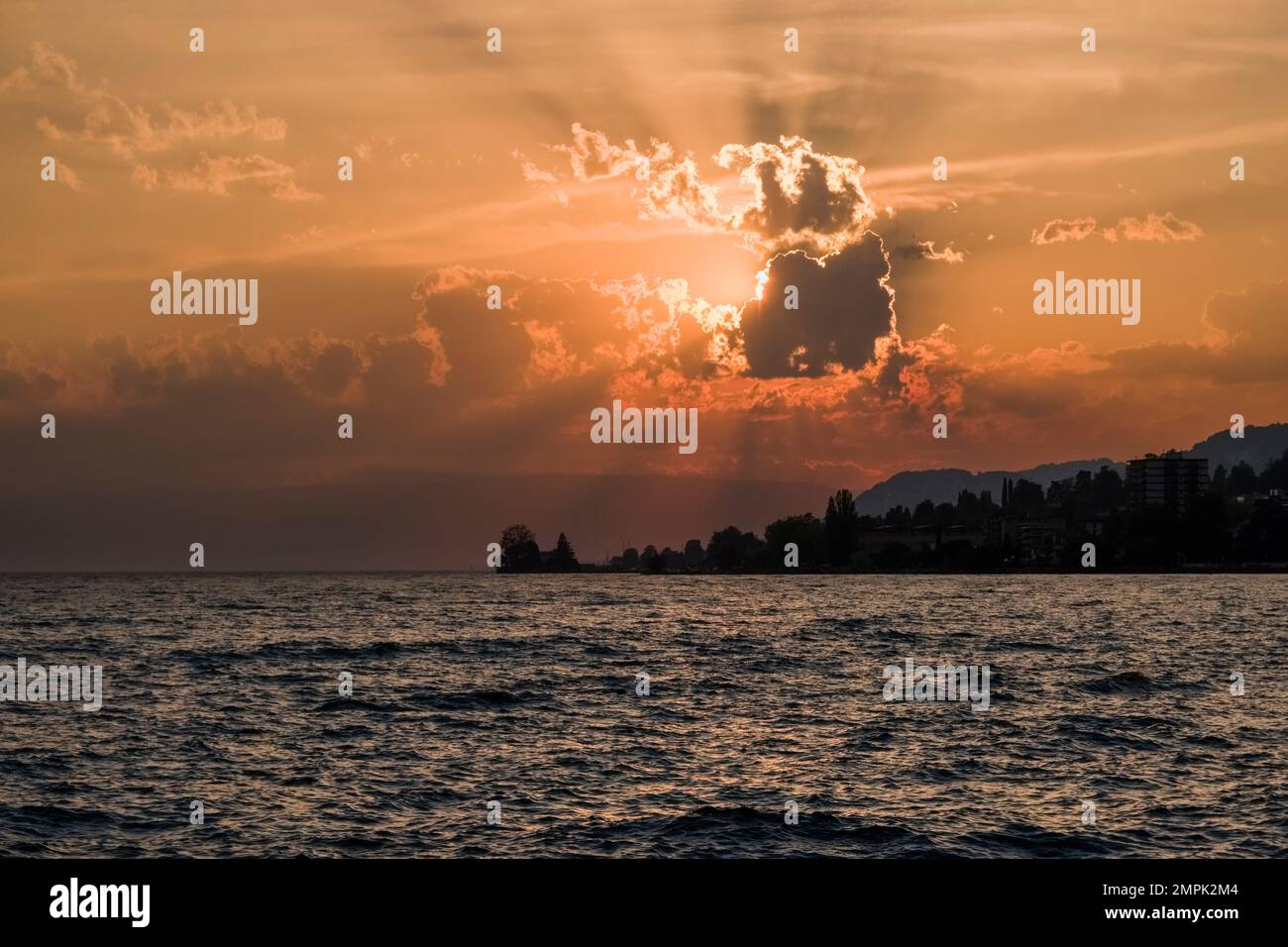 Tramonto sul Lago di Ginevra, alberi e paesaggi alpini in lontananza. Foto Stock