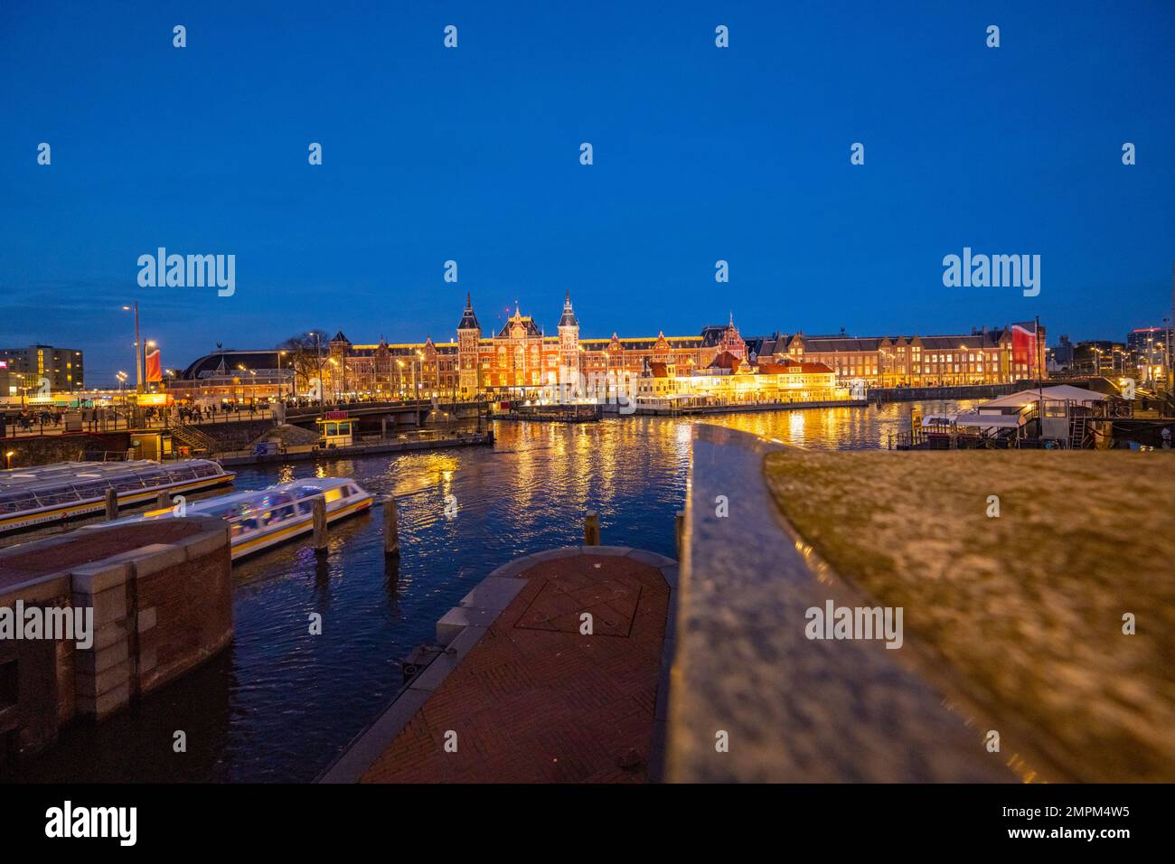 La parte anteriore della stazione centrale di Amsterdam IJzijde dall'altra parte del porto da via Prins Hendrikkade di notte. Foto Stock