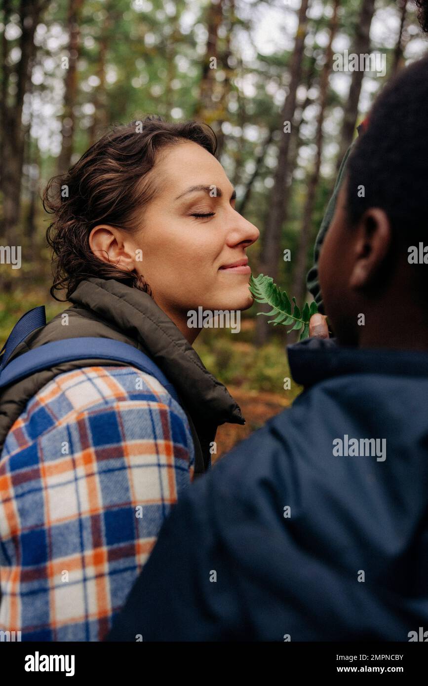 Figlio che tocca la foglia sul volto sorridente della madre con gli occhi chiusi nella foresta Foto Stock