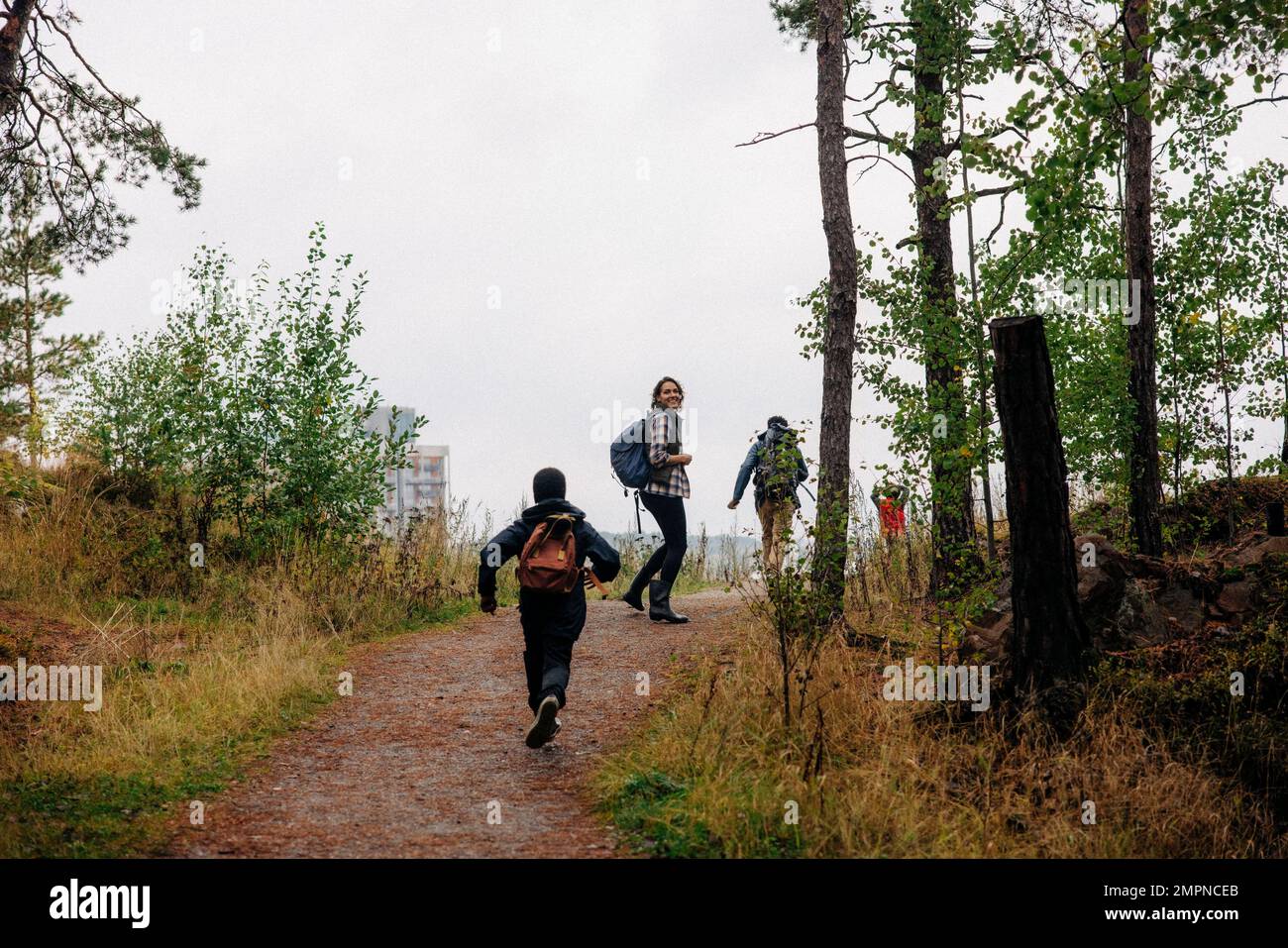 Vista posteriore del figlio che corre verso la madre sul sentiero mentre escursioni nella foresta Foto Stock