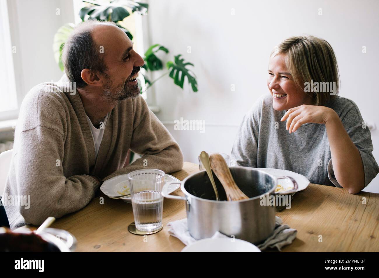 Coppia matura felice che parla l'un l'altro seduto al tavolo da pranzo in casa Foto Stock