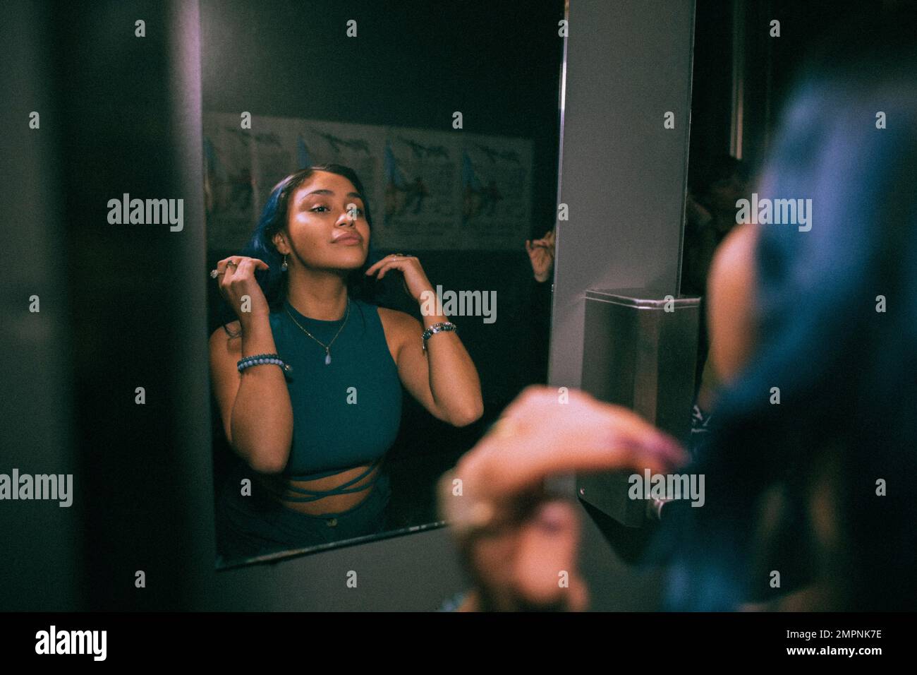 Riflesso della giovane donna che guarda lo specchio riflesso nella stanza da bagno del nightclub Foto Stock