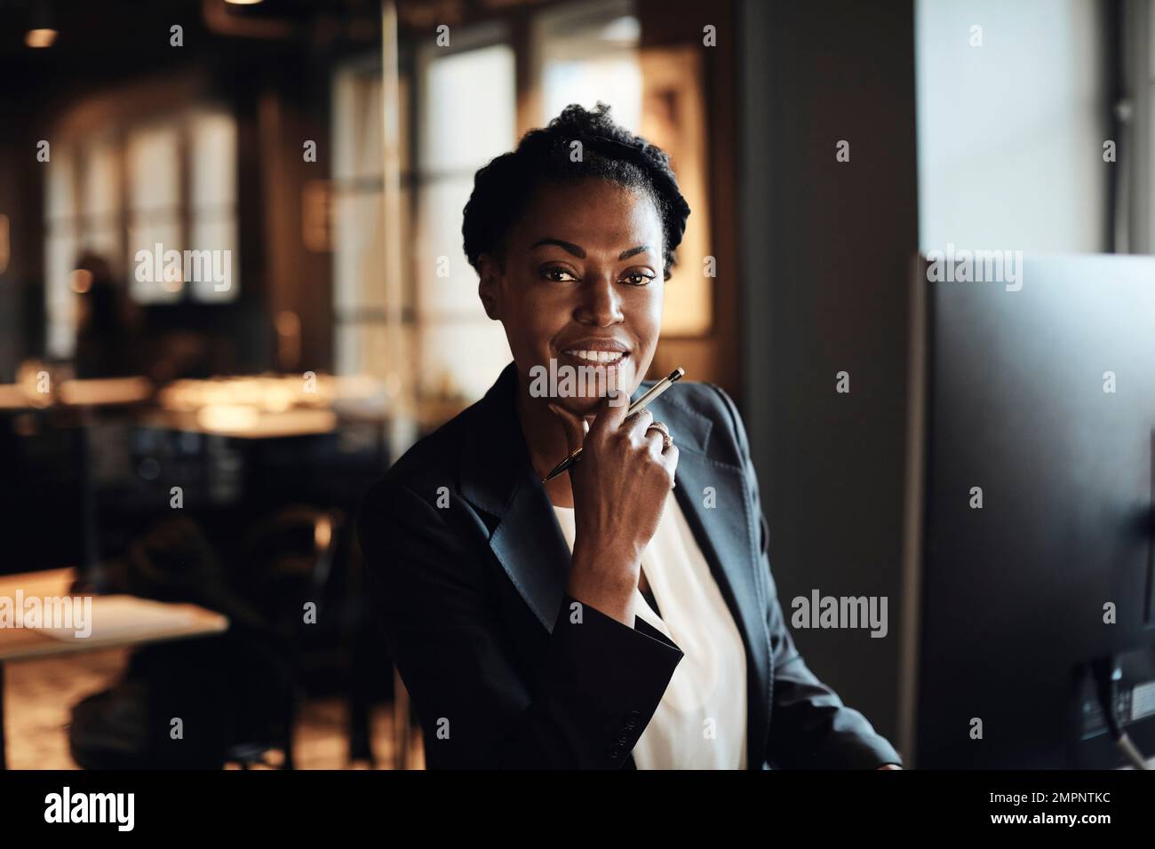 Donna d'affari matura sorridente con mano sul mento in ufficio Foto Stock