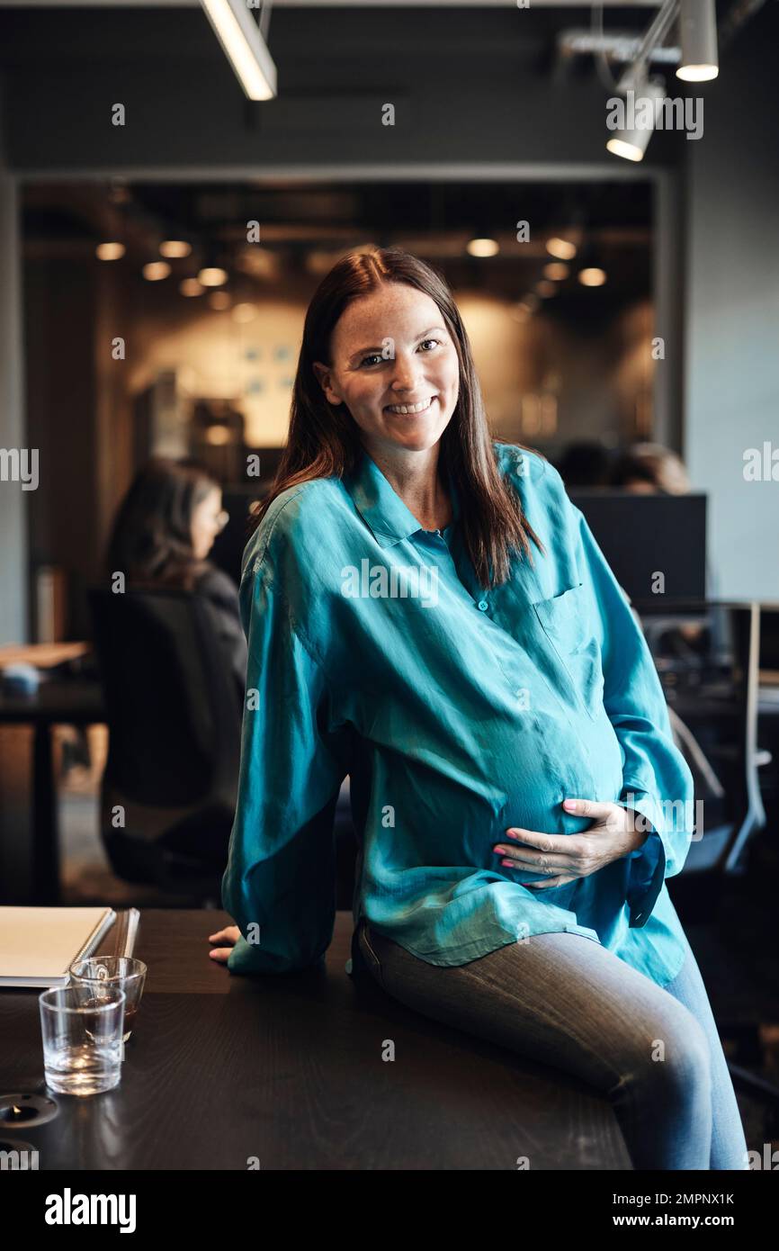 Ritratto di una donna d'affari incinta seduta alla scrivania in ufficio Foto Stock