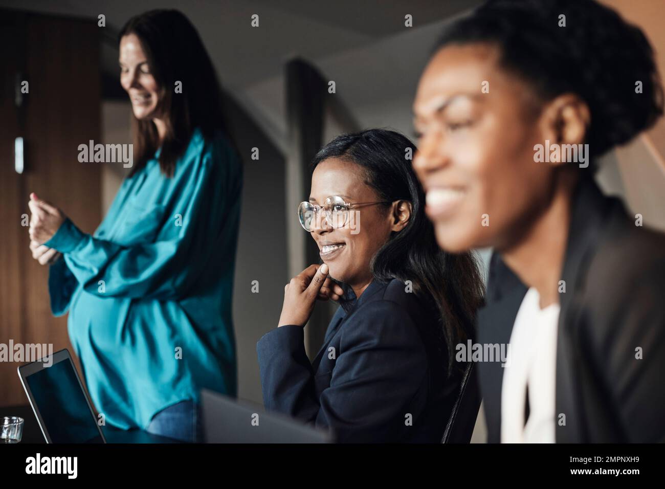 Donna d'affari sorridente con mano sul mento da parte dei colleghi durante la riunione in ufficio Foto Stock
