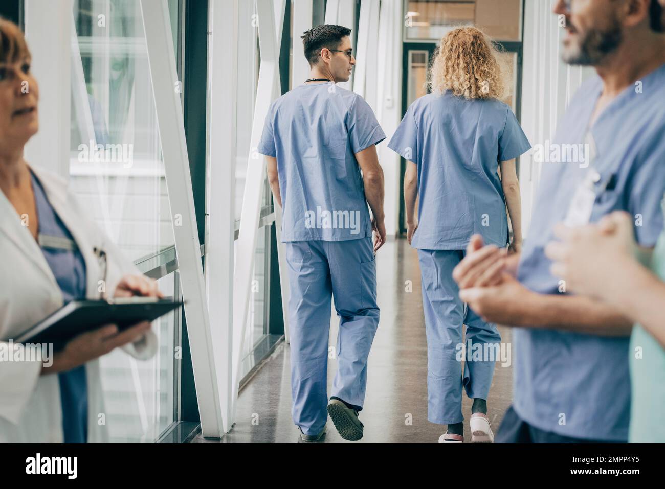 Vista posteriore degli operatori sanitari maschili e femminili che camminano nel corridoio Foto Stock