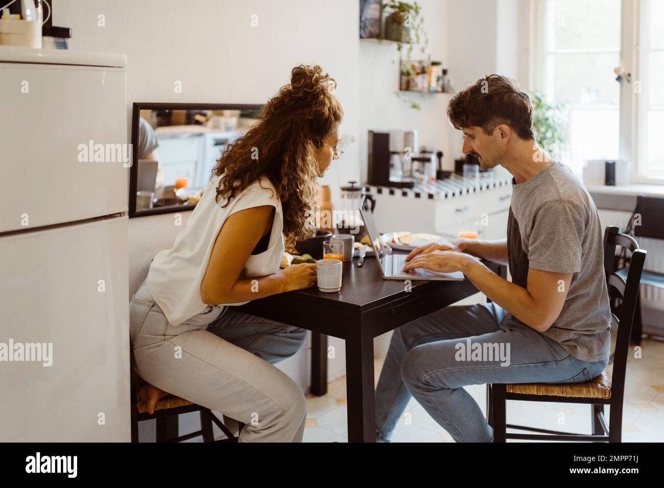 Uomo che parla con una donna mentre usa un computer portatile sul tavolo da pranzo a casa Foto Stock