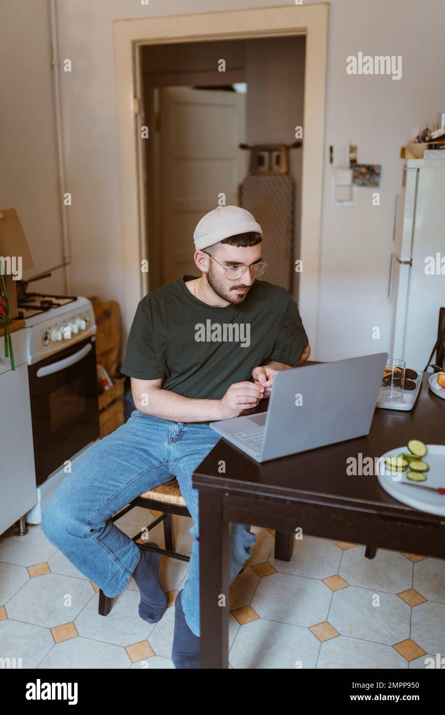 Uomo che usa un computer portatile sul tavolo da pranzo seduto in cucina a casa Foto Stock