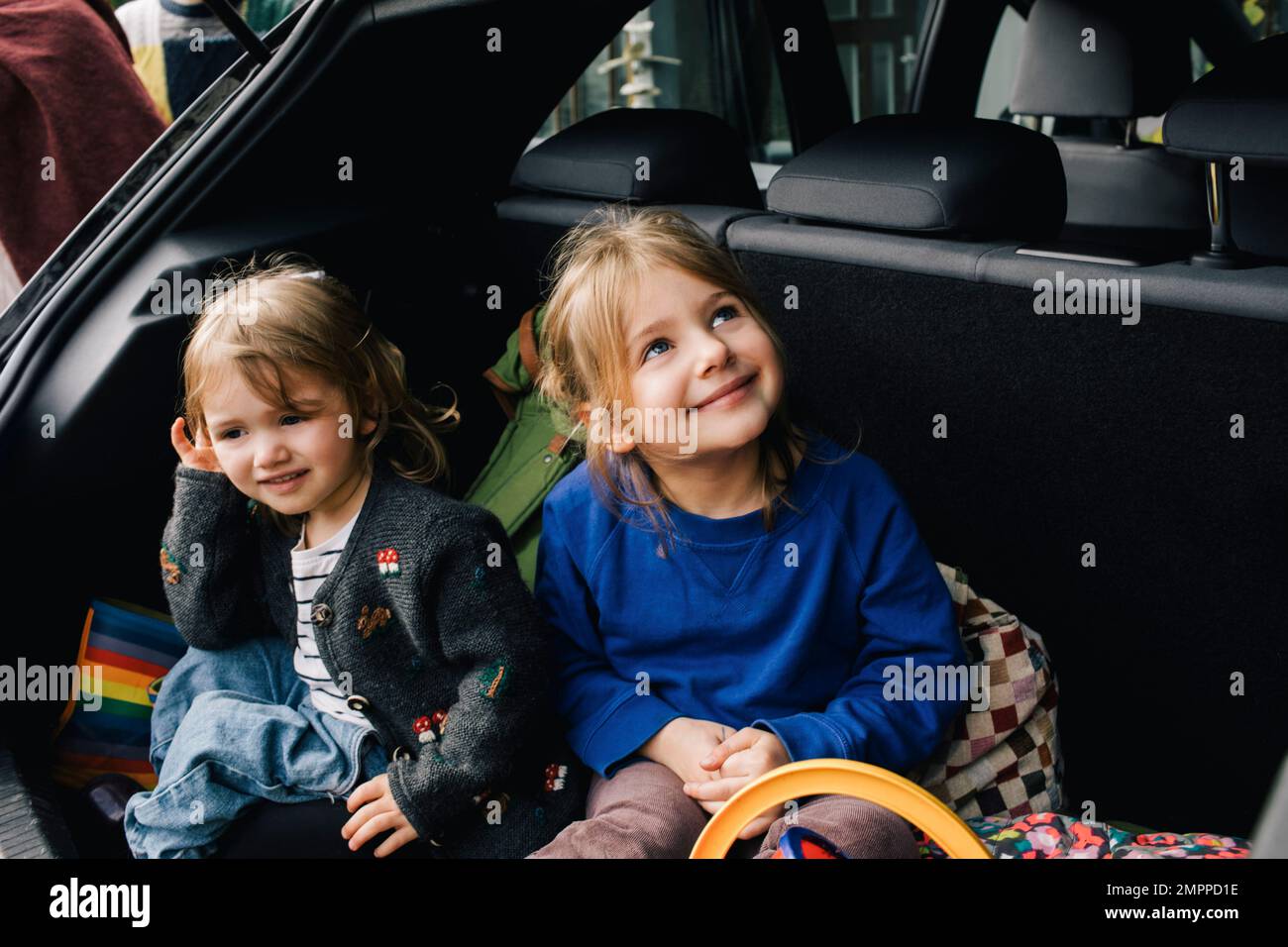 Ragazze sorridenti che si siedono insieme nel bagagliaio dell'automobile elettrica Foto Stock