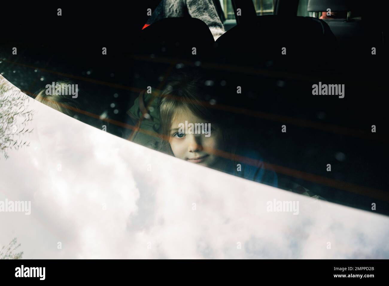 Ritratto di ragazza seduta nel bagagliaio dell'automobile elettrica visto attraverso il parabrezza posteriore Foto Stock