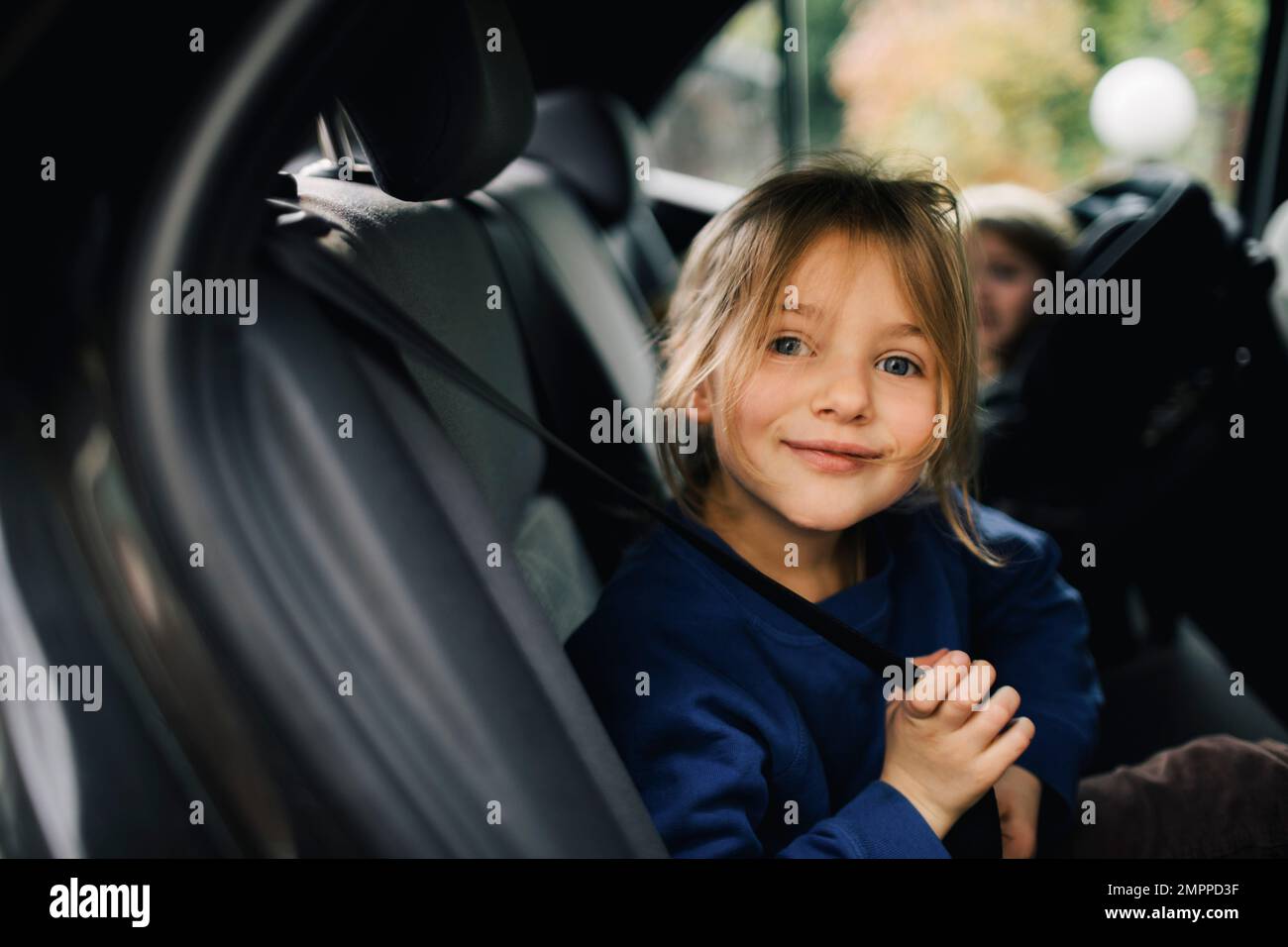 Ritratto di una ragazza sorridente che tiene la cintura di sicurezza mentre si siede in auto Foto Stock