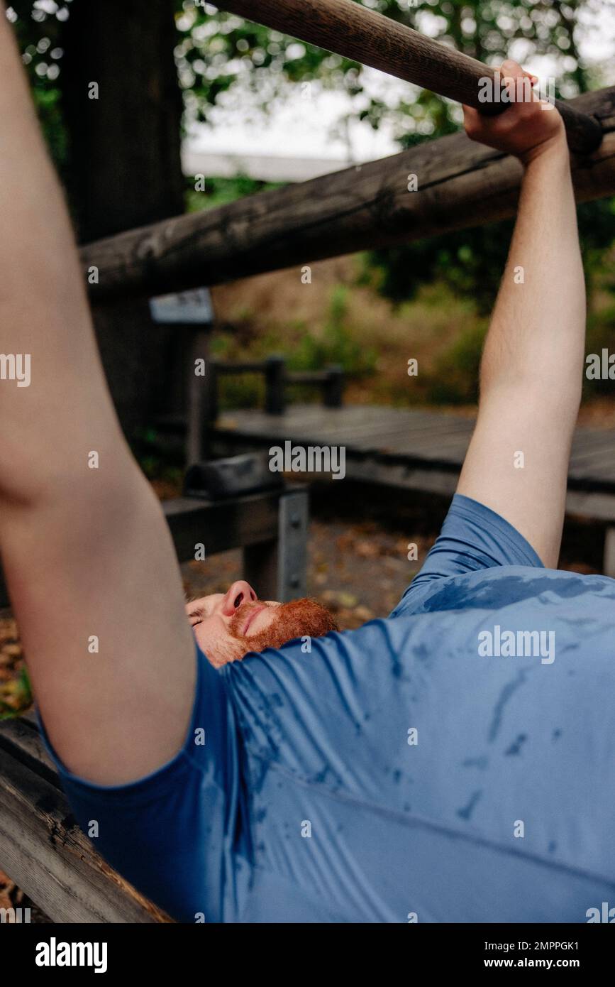 Uomo in sovrappeso che fa la pressa del banco mentre esercitandosi al parco Foto Stock