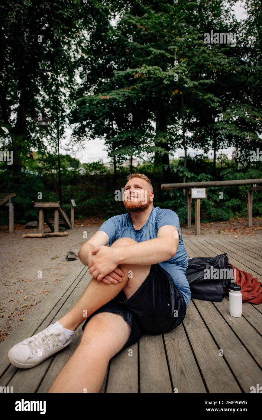 Un uomo in sovrappeso sogna mentre si siede su una panca al parco Foto Stock