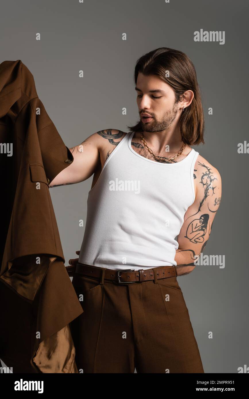 Uomo dai capelli lunghi con giacca da tatuaggio isolata sul grigio Foto Stock