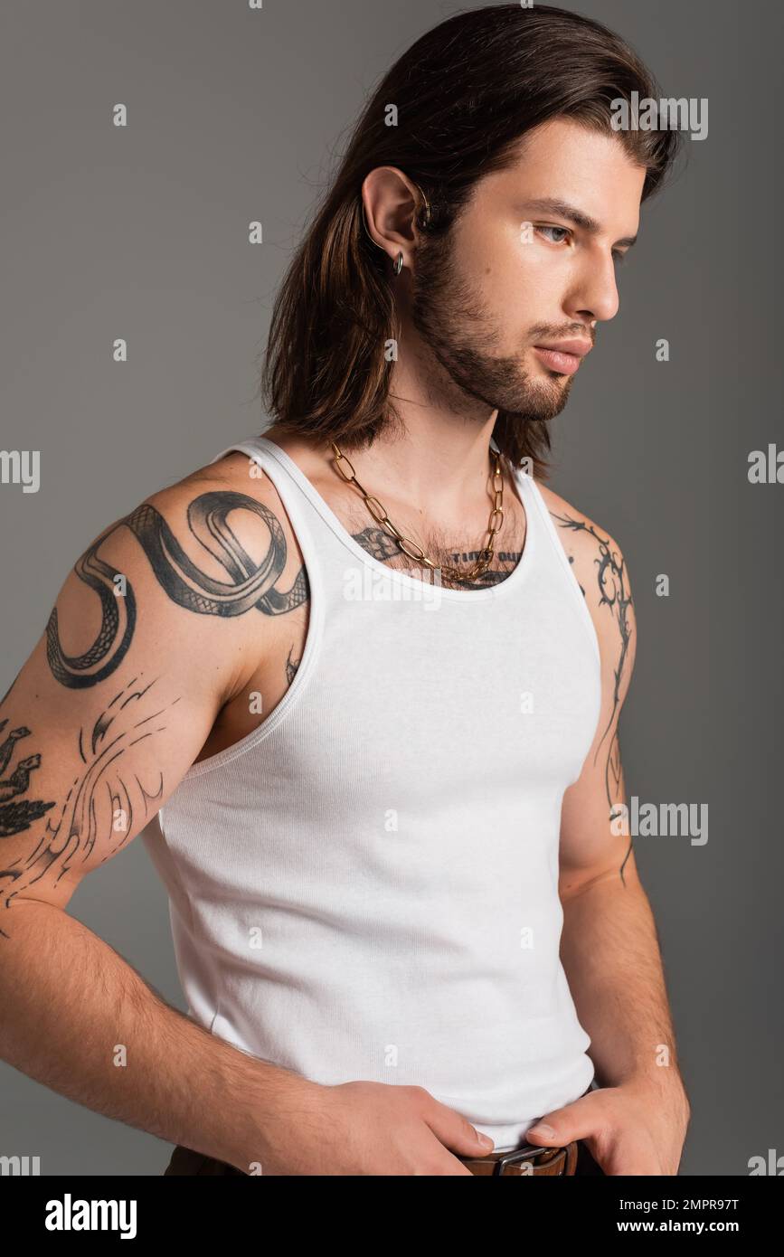 Uomo dai capelli lunghi con tatuaggio sul corpo che posa isolato sul grigio Foto Stock