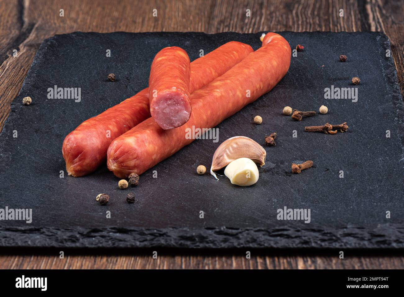 Tavola da servizio in pietra con sottili salsicce affumicate e spezie. Primo piano, sfondo in legno. Foto Stock