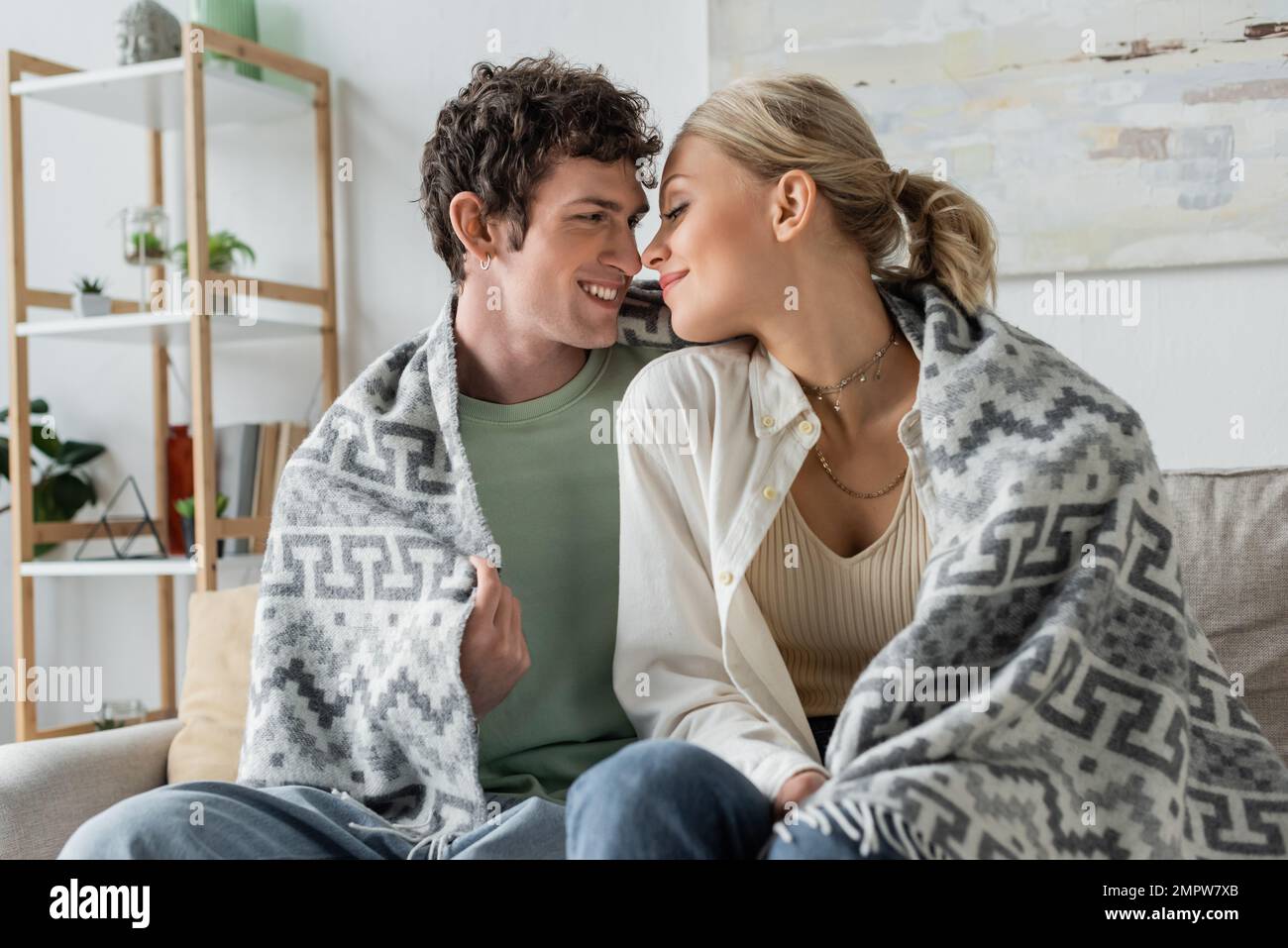felice giovane uomo e donna bionda sorridente coperto di coperta seduta sul divano, immagine stock Foto Stock