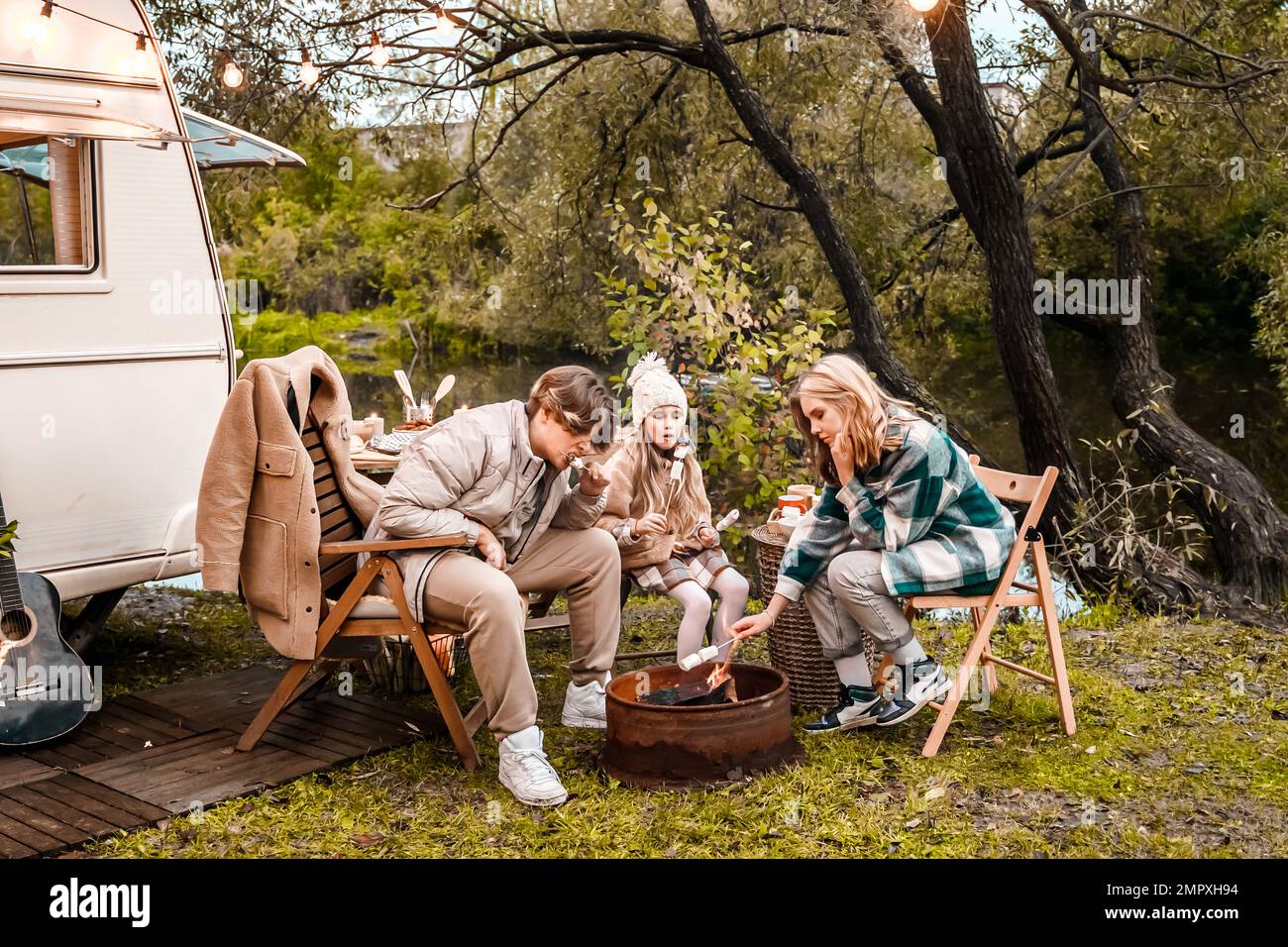 Bambini, famiglia, sorella fratello friggere marshmallows sul fuoco. Picnic nella natura. Sedia di legno, table.barbecue barbecue cibo. Viaggio di vacanza, fine settimana di vacanza dinne Foto Stock