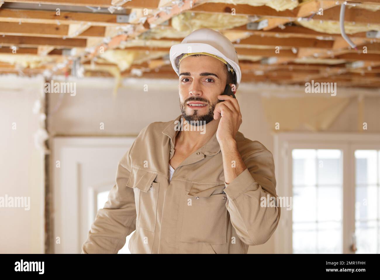 giovane costruttore maschile che utilizza lo smartphone in una struttura di ristrutturazione Foto Stock